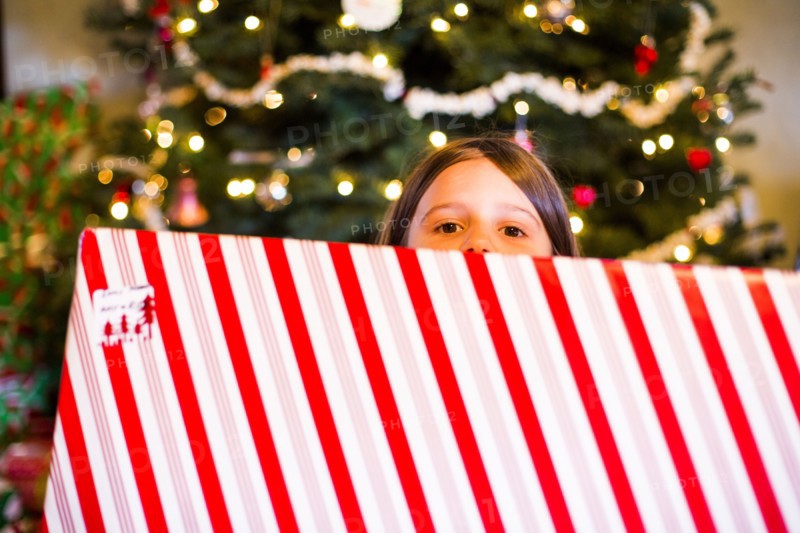 Caucasian girl holding wrapped Christmas gift near tree