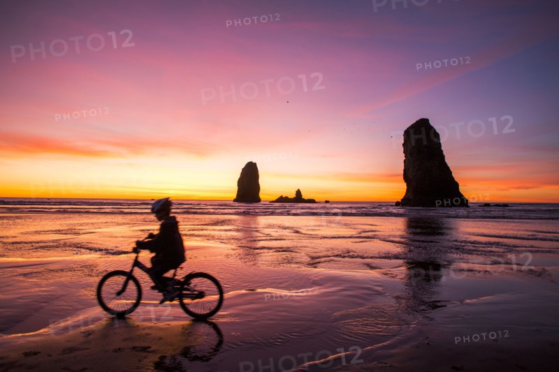 Silhouette of Caucasian girl biking near rock formations on Cannon Beach