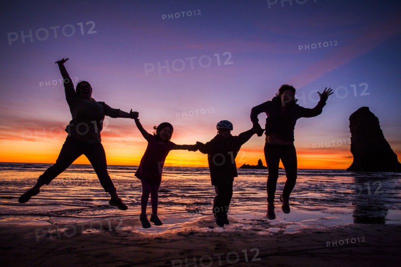 Silhouette of Caucasian family jumping for joy on Cannon Beach