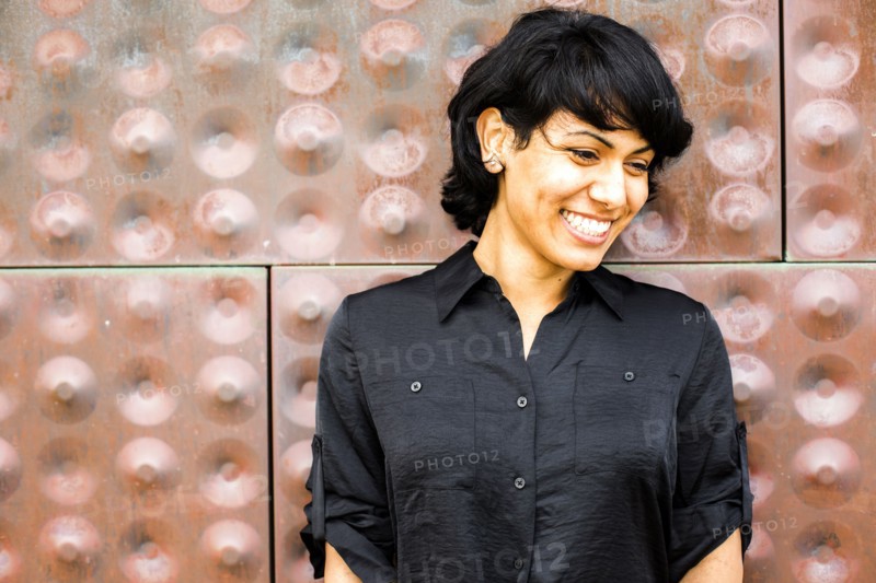 Hispanic woman smiling near metal wall