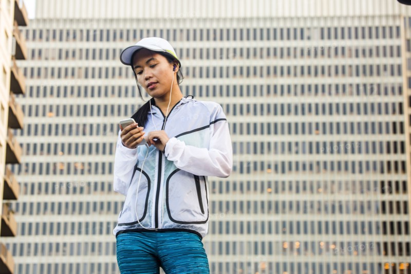 Asian runner using cell phone near highrise building