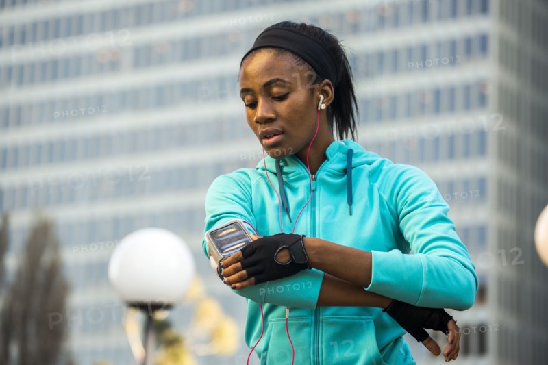 Black runner using cell phone near high rise buildings