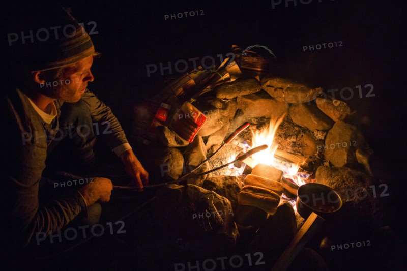 Caucasian man roasting food over campfire