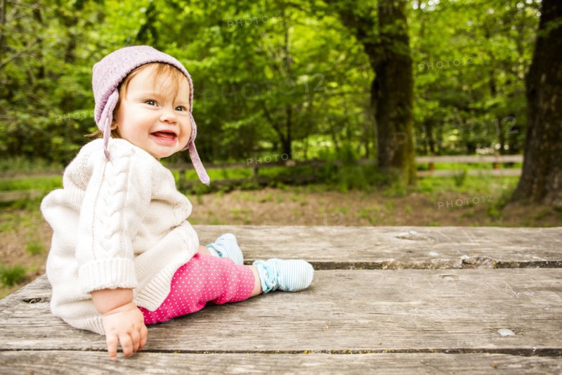 Caucasian baby girl sitting on picnic table in forest