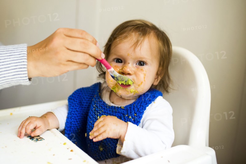 Mother feeding baby girl in high chair