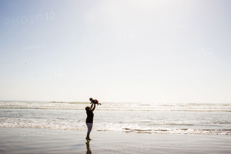 Caucasian mother lifting baby daughter on beach