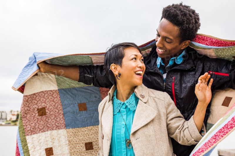 Couple wrapping themselves in blanket outdoors