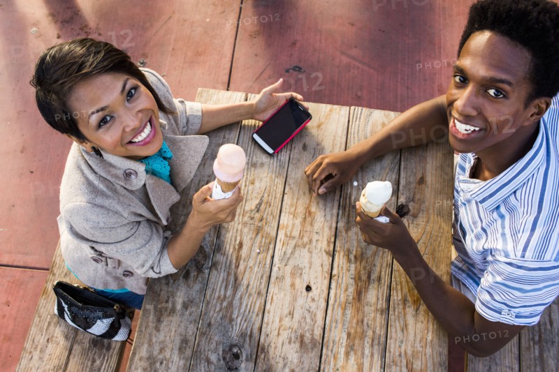 Couple eating ice cream and using cell phone at picnic table