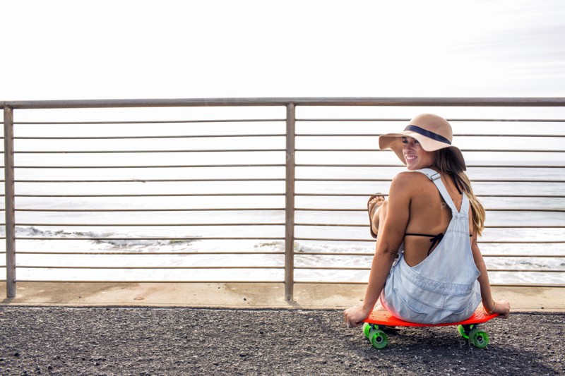 Caucasian woman sitting on skateboard at beach