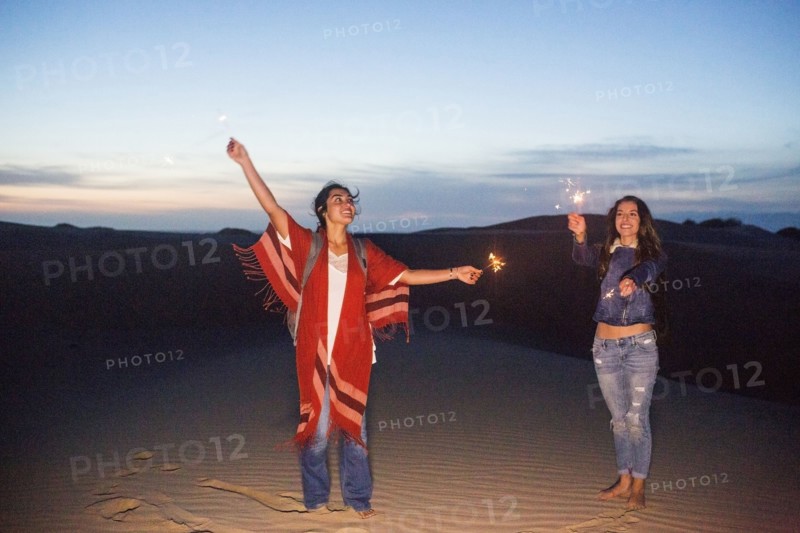 Mixed race women playing with sparklers on sand dunes