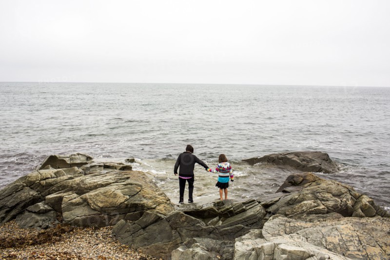 Caucasian mother and daughter holding hands on rocks at ocean