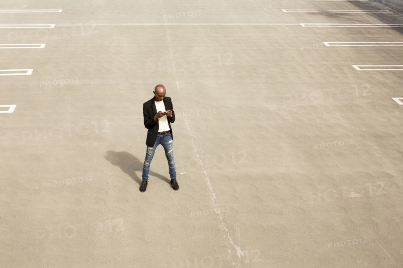 Gay Black man texting in empty parking lot