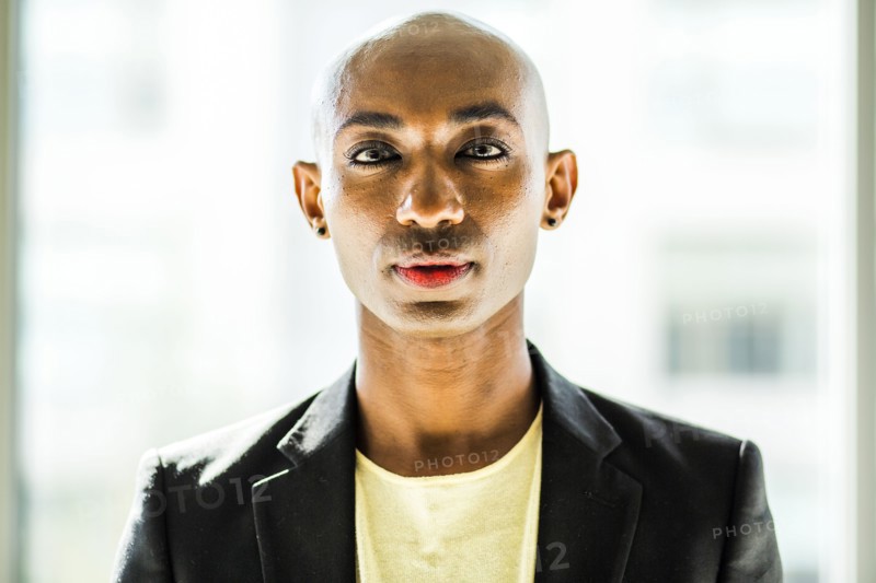 Serious gay Black man posing near window