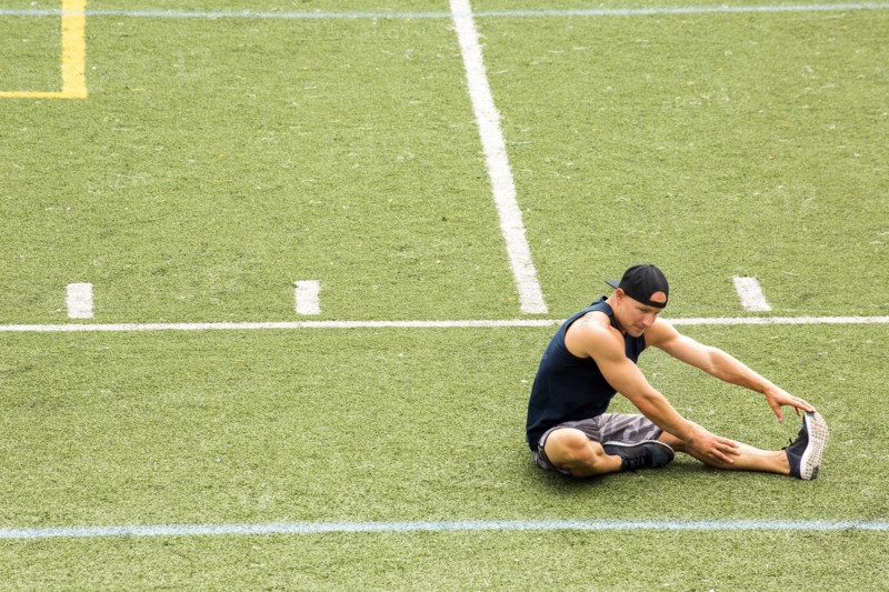 Caucasian man sitting on sports field stretching leg