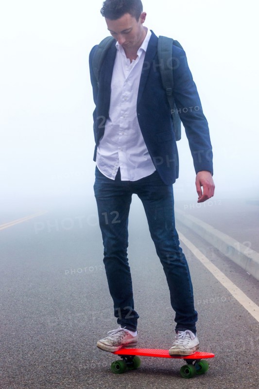 Caucasian man standing on small red skateboard in fog