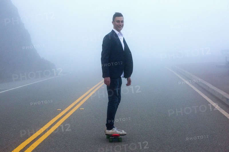 Caucasian man standing on small red skateboard in fog