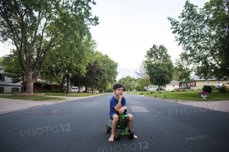 Pensive mixed race boy sitting on toy tractor in street