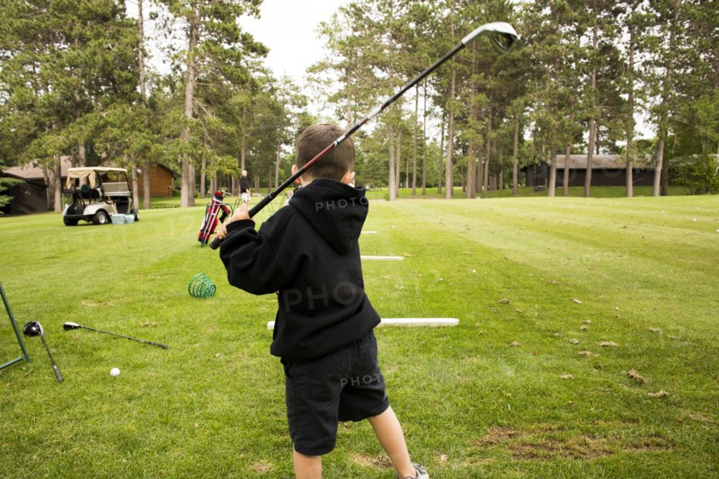 Mixed race boy swinging golf club