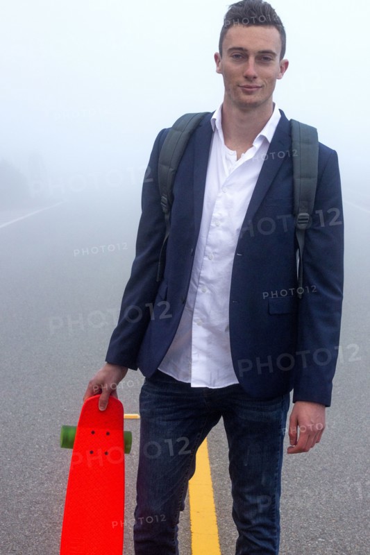 Caucasian man holding small red skateboard in fog