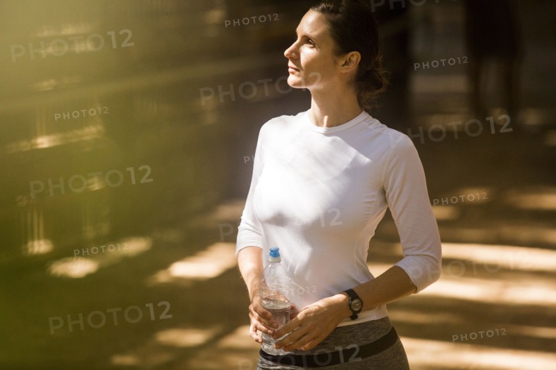 Pensive woman holding water bottle in sunny forest