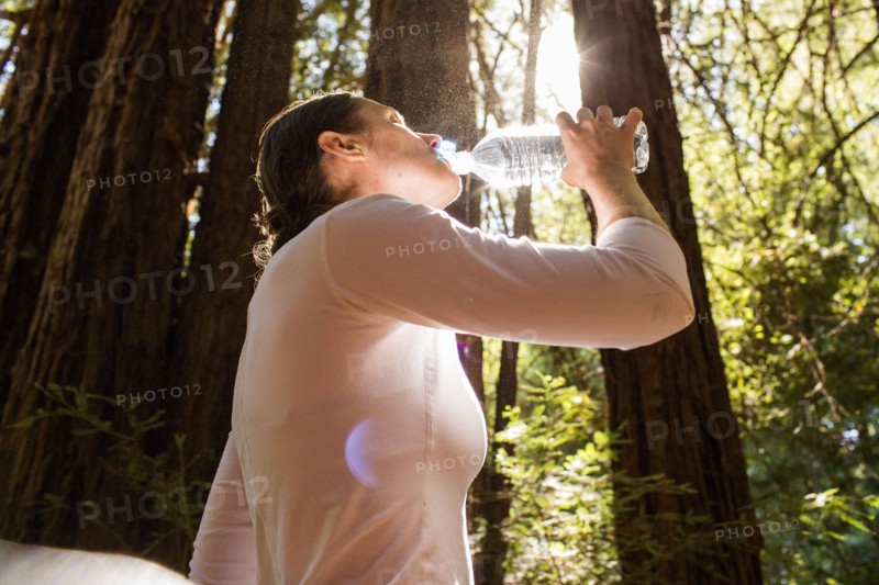 Woman drinking water from bottle in sunny forest