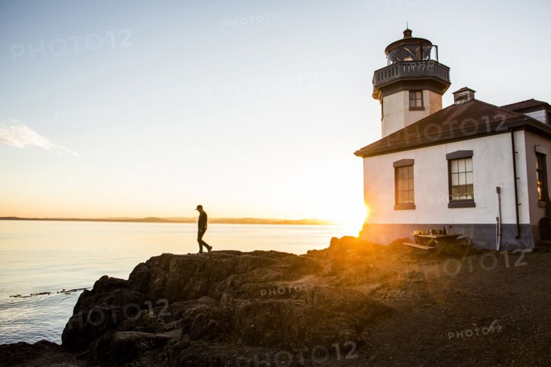Silhouette of Caucasian man walking on rocks near lighthouse