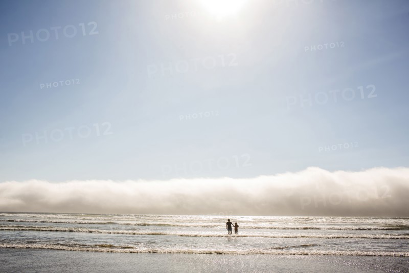 Caucasian mother and son wading in ocean waves at beach