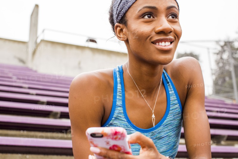 Smiling Black woman sitting on bleachers texting on cell phone