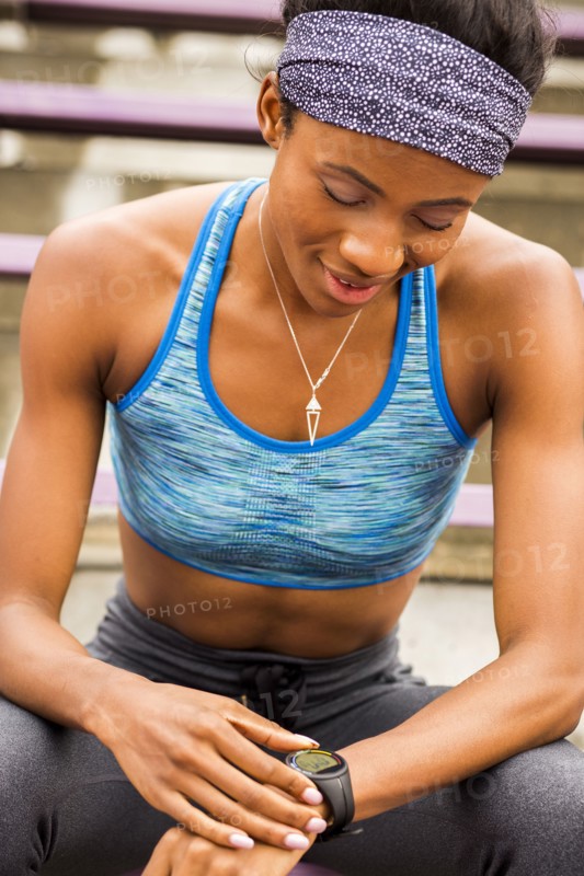 Black woman sitting on bleachers checking smart watch