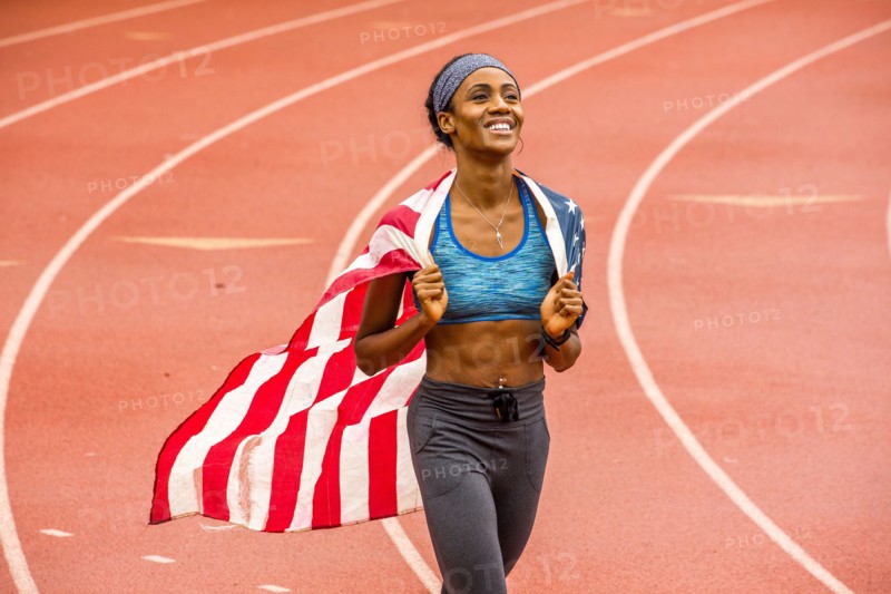 Smiling Black athlete holding American flag on track