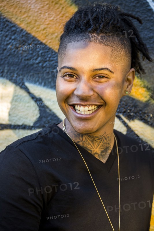 Portrait of androgynous Mixed Race woman smiling near graffiti wall