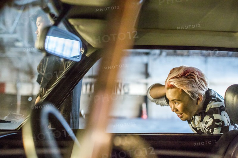 Androgynous Asian woman checking hair in side-view mirror