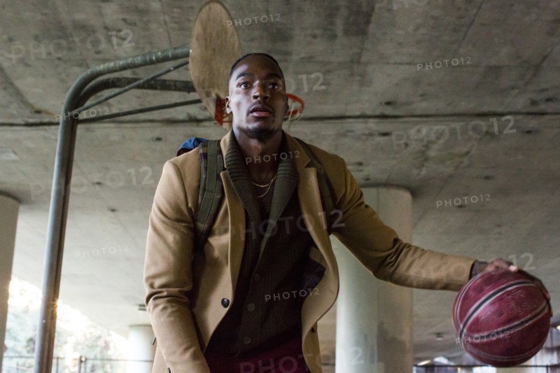 Black man wearing backpack playing basketball under overpass