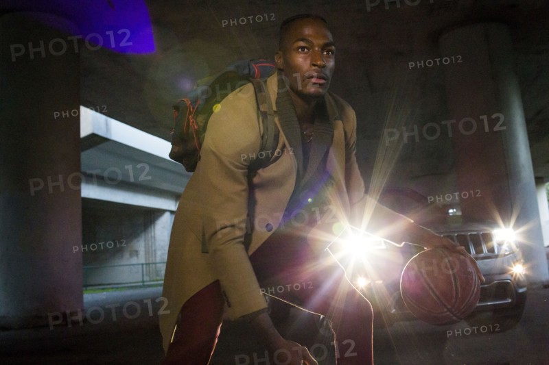 Headlights shining on Black man wearing backpack playing basketball