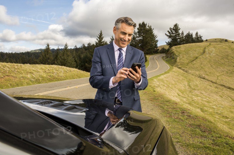 Smiling Caucasian businessman near car texting on cell phone