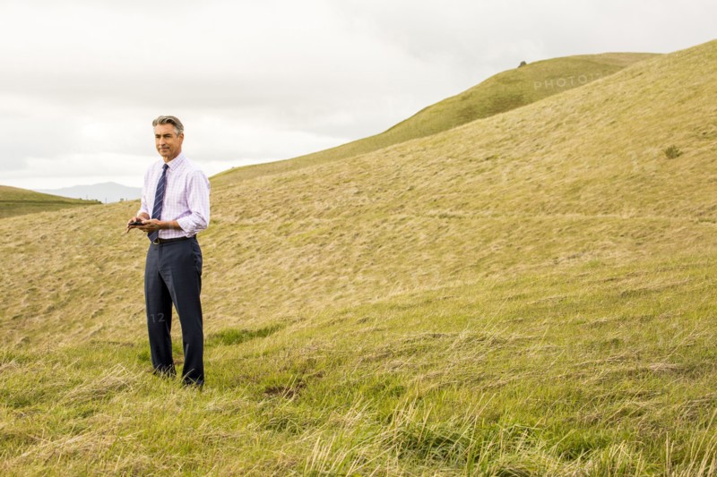 Serious Caucasian businessman standing in grass holding cell phone