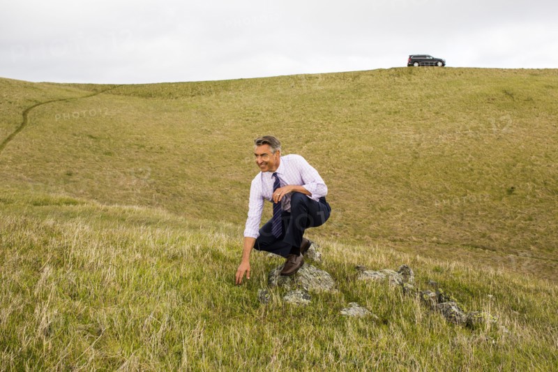 Smiling Caucasian businessman crouching in grass
