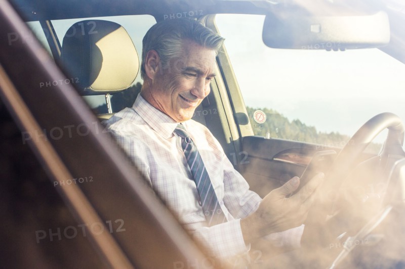 Smiling Caucasian businessman sitting in car texting on cell phone