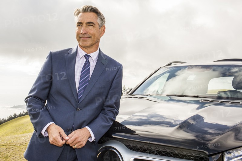 Smiling Caucasian businessman leaning on car