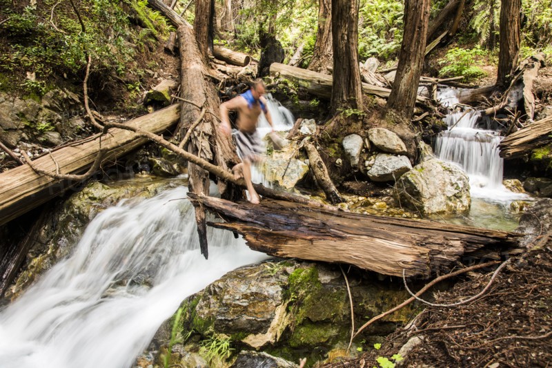 Caucasian man walking over waterfall on log in woods