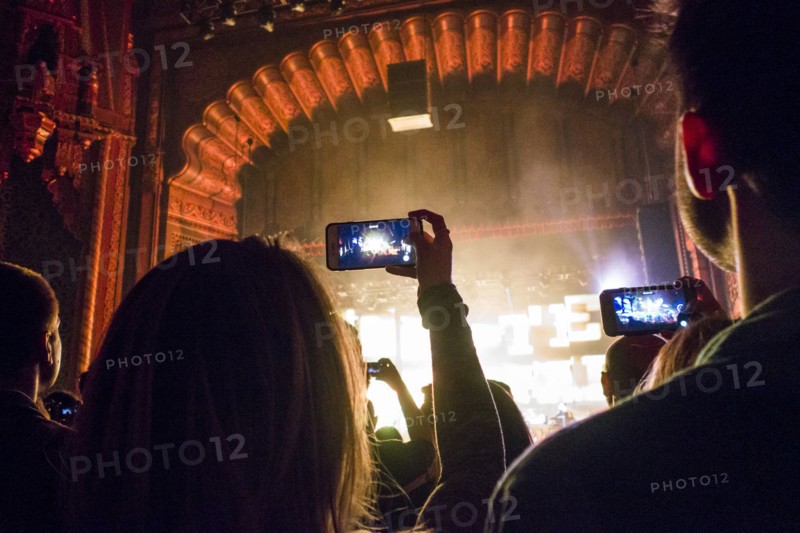 People photographing with cell phones at concert in theater