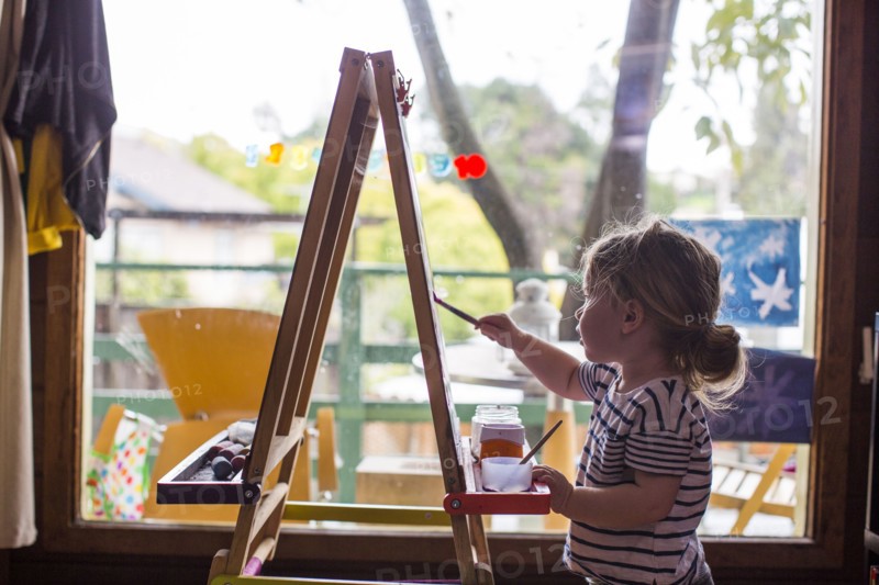 Caucasian girl painting on easel near window