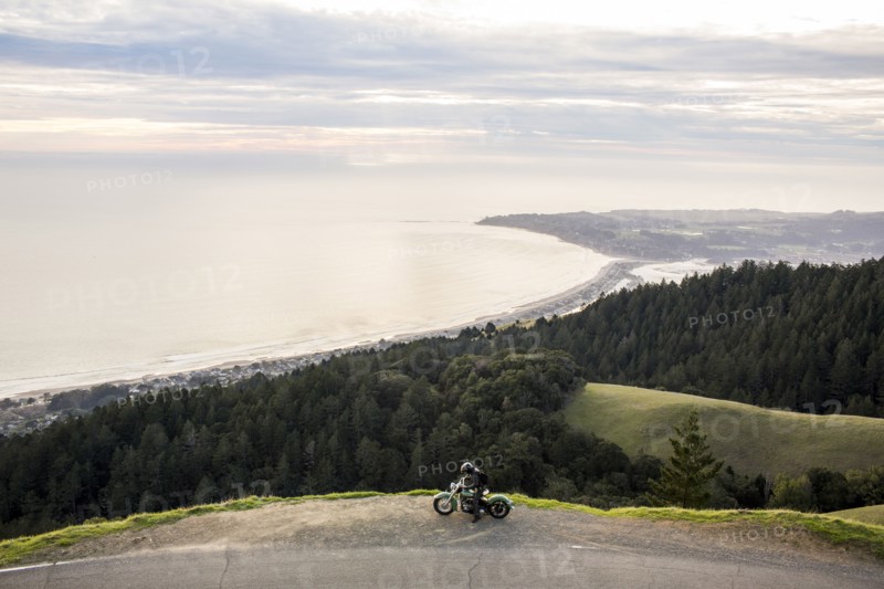 Person with motorcycle at edge of cliff near ocean