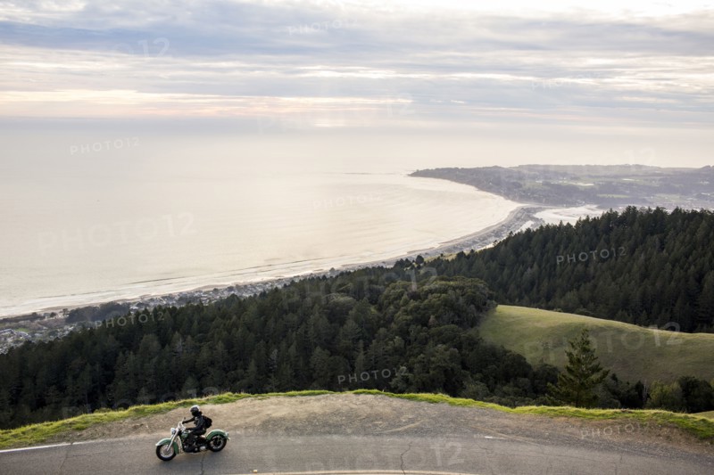Person riding motorcycle at edge of cliff near ocean