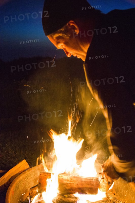 Caucasian man stoking campfire at night