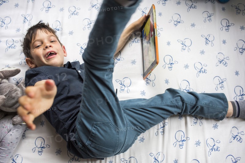 Playful Mixed Race boy laying on bed holding digital tablet