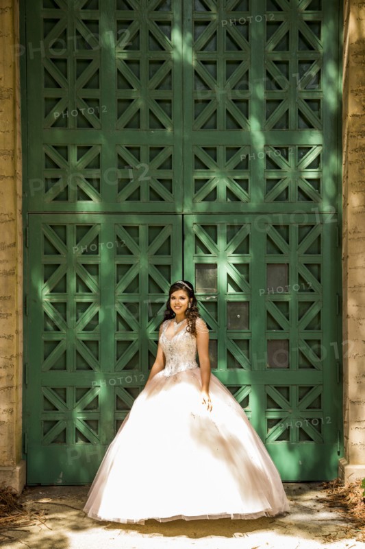 Smiling Hispanic girl wearing gown near green wall
