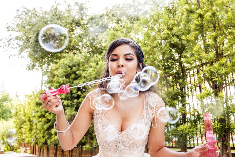 Hispanic girl wearing gown blowing bubbles