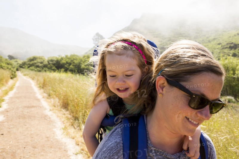 Caucasian mother carrying daughter while hiking