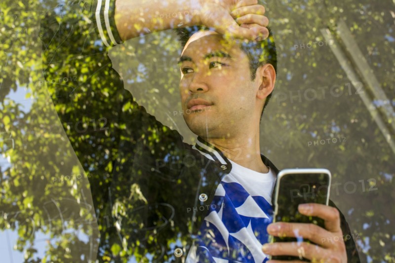 Serious Chinese man leaning on window holding cell phone